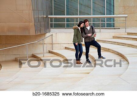 Young couple looking digital tablet in the city, digital tablet, Guggenheim Museum, Abandoibarra, Bilbao, Bizkaia, Basque Country, Spain View Large Photo Image Stock Photography - Young couple looking digital tablet in the city, digital tablet, Guggenheim Museum, Abandoibarra, Bilbao, Bizkaia, Basque Country, Spain. Fotosearch