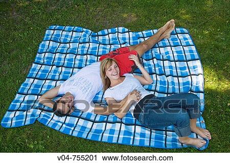 Stock Image - Young couple lying on a blanket in the garden, smiling. Fotosearch