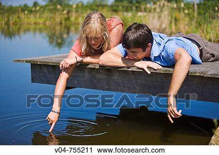 Young couple lying on a footbridge at a lake making bubbles View Large Photo Image Stock Image - Young couple lying on a footbridge at a lake making bubbles. Fotosearch