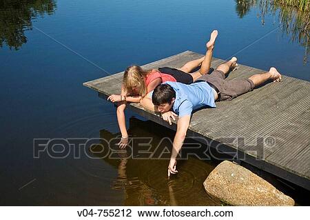 Young couple lying on a footbridge at a lake making bubbles View Large Photo Image Stock Image - Young couple lying on a footbridge at a lake making bubbles. Fotosearch