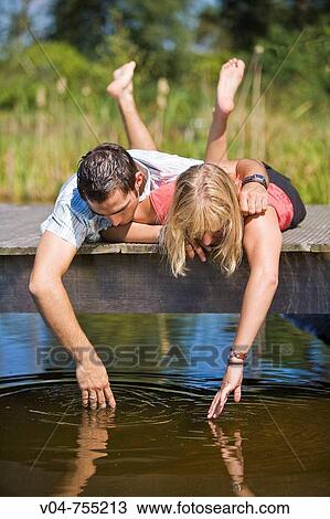 Young couple lying on a footbridge at a lake looking into the water View Large Photo Image Stock Image - Young couple lying on a footbridge at a lake looking into the water. Fotosearch