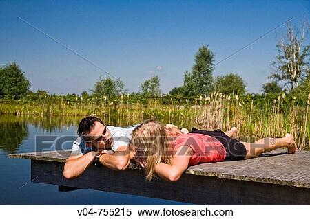 Young couple lying on a footbridge at a lake relaxing View Large Photo Image Stock Photography - Young couple lying on a footbridge at a lake relaxing. Fotosearch