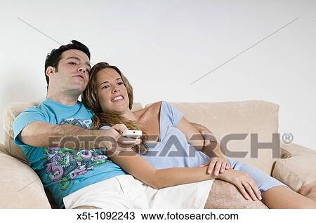 young couple on Sofa watching Television Holding a remote control and zapping channels Model Release available View Large Photo Image Stock Image - young couple on Sofa watching Television Holding a remote control and zapping channels Model Release available. Fotosearch