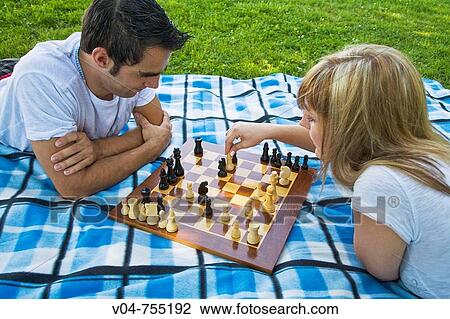 Stock Image - Young couple playing chess in the garden. Fotosearch
