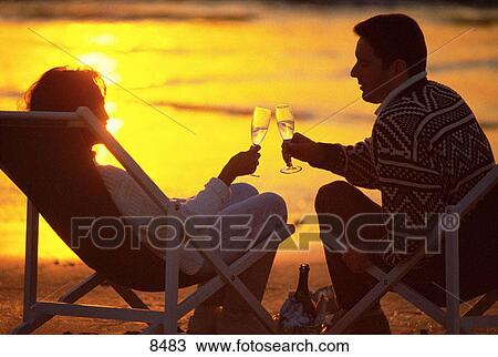 Stock Image - Young couple relaxing sharing a drink at the beach. Fotosearch