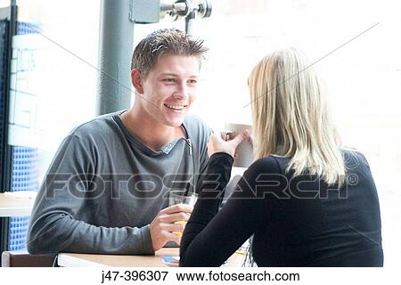 Young couple, sitting facing each other, in a cafe, having a drink, smiling at each other View Large Photo Image Stock Photo - Young couple, sitting facing each other, in a cafe, having a drink, smiling at each other. Fotosearch