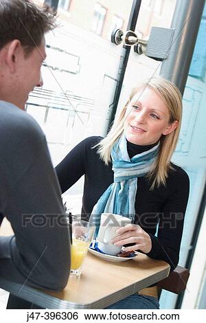 Young couple, sitting facing each other, in a cafe, having a drink, smiling at each other View Large Photo Image Stock Photograph - Young couple, sitting facing each other, in a cafe, having a drink, smiling at each other. Fotosearch