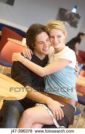 Young couple sitting in a cafe cuddling, she? s sitting on his knee View Large Photo Image Stock Photo - Young couple sitting in a cafe cuddling, she? s sitting on his knee. Fotosearch