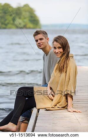Young couple sitting in a pier, smiling at camera View Large Photo Image Picture - Young couple sitting in a pier, smiling at camera. Fotosearch
