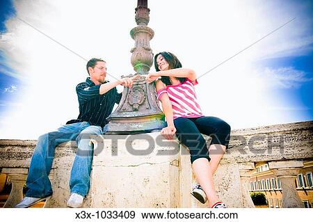 Young couple sitting near lamp post touching fingers together, Rome, Italy View Large Photo Image Stock Photo - Young couple sitting near lamp post touching fingers together, Rome, Italy. Fotosearch