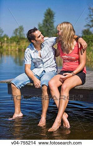 Young couple sitting on a footbridge at a lake looking at each other View Large Photo Image Picture - Young couple sitting on a footbridge at a lake looking at each other. Fotosearch