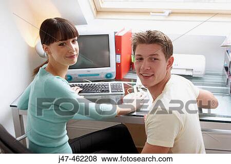 Stock Photo - Young couple sitting together in the office, smiling off camera.. Fotosearch