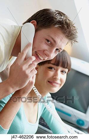 young couple sitting together in the office hes on the phone both smiling to camera View Large Photo Image Stock Photograph - young couple sitting together in the office hes on the phone both smiling to camera. Fotosearch