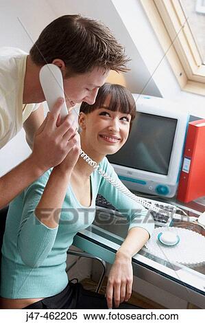 young couple sitting together in the office hes on the phone both smiling at each other View Large Photo Image Stock Photography - young couple sitting together in the office hes on the phone both smiling at each other. Fotosearch