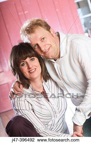 Young couple sitting together smiling into camera View Large Photo Image Stock Image - Young couple sitting together smiling into camera. Fotosearch