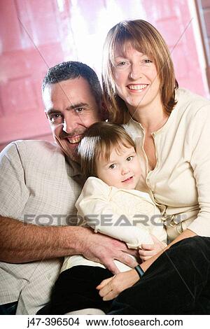 Young couple sitting together with their 3 year old daughter, smiling into camera View Large Photo Image Picture - Young couple sitting together with their 3 year old daughter, smiling into camera. Fotosearch