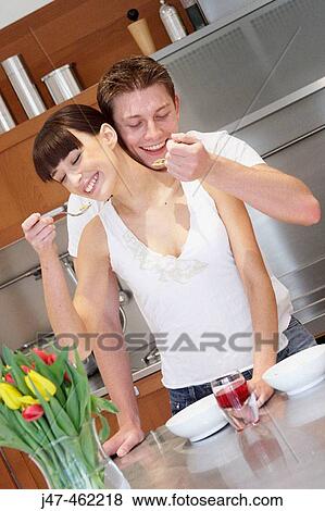 Young couple standing together in the kitchen eating breakfast, smiling View Large Photo Image Stock Photo - Young couple standing together in the kitchen eating breakfast, smiling. Fotosearch