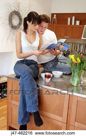 Young couple standing together in the kitchen eating breakfast, looking at a book. View Large Photo Image Stock Photograph - Young couple standing together in the kitchen eating breakfast, looking at a book.. Fotosearch
