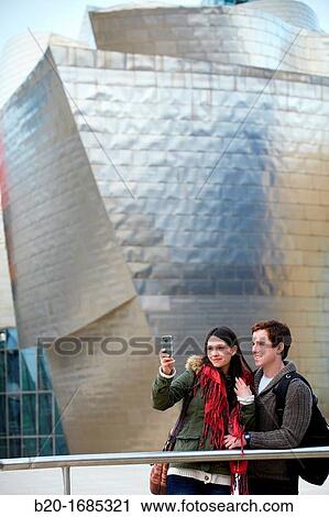 Young couple taking pictures with mobile phone in the city, smartphone, Guggenheim Museum, Abandoibarra, Bilbao, Bizkaia, Basque Country, Spain View Large Photo Image Stock Image - Young couple taking pictures with mobile phone in the city, smartphone, Guggenheim Museum, Abandoibarra, Bilbao, Bizkaia, Basque Country, Spain. Fotosearch