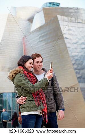 Young couple taking pictures with mobile phone in the city, smartphone, Guggenheim Museum, Abandoibarra, Bilbao, Bizkaia, Basque Country, Spain View Large Photo Image Stock Image - Young couple taking pictures with mobile phone in the city, smartphone, Guggenheim Museum, Abandoibarra, Bilbao, Bizkaia, Basque Country, Spain. Fotosearch