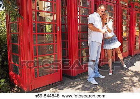 Young couple using mobile phones on street next to row of British public phone boxes. View Large Photo Image Stock Photo - Young couple using mobile phones on street next to row of British public phone boxes.. Fotosearch
