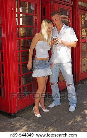 Young couple using mobile phones on street next to row of British public phone boxes. View Large Photo Image Stock Photo - Young couple using mobile phones on street next to row of British public phone boxes.. Fotosearch