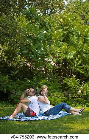Young couple using their cell phones in the garden, sitting on a blanket View Large Photo Image Stock Image - Young couple using their cell phones in the garden, sitting on a blanket. Fotosearch