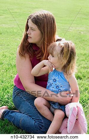 Young daughter sitting on her mother's lap at the park View Large Photo Image Picture - Young daughter sitting on her mother's lap at the park. Fotosearch