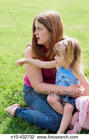 Young daughter sitting on her mother's lap at the park View Large Photo Image Stock Image - Young daughter sitting on her mother's lap at the park. Fotosearch