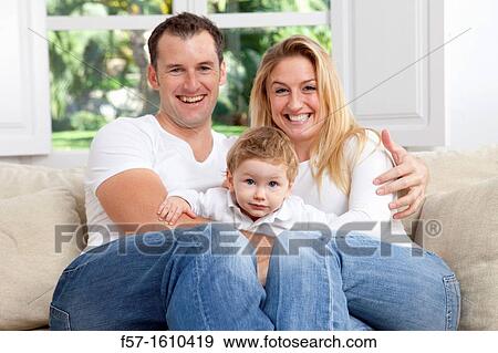 Stock Photo - Young family sitting on their sofa at home. Fotosearch