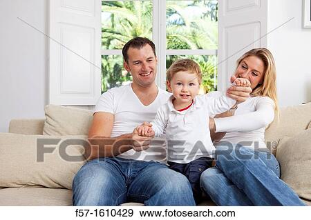 Stock Photo - Young family sitting on their sofa at home. Fotosearch