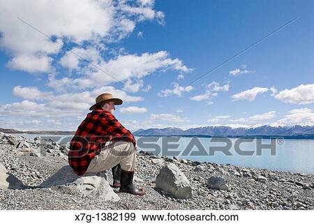 Stock Photo - Young farmer looking out at Lake Pukaki, South Island of New Zealand. Fotosearch