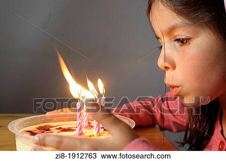 Stock Image - Young girl blows candles on a birthday cake. Fotosearch