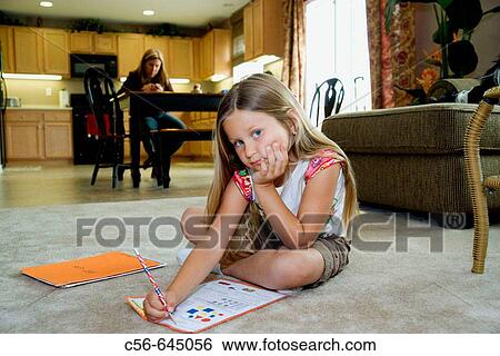 Stock Photograph - Young girl does her homework, mother in background. Fotosearch