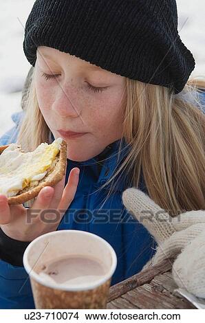 Young girl eating a sandwich and drinking hot chocolate outdoors in the winter View Large Photo Image Picture - Young girl eating a sandwich and drinking hot chocolate outdoors in the winter. Fotosearch