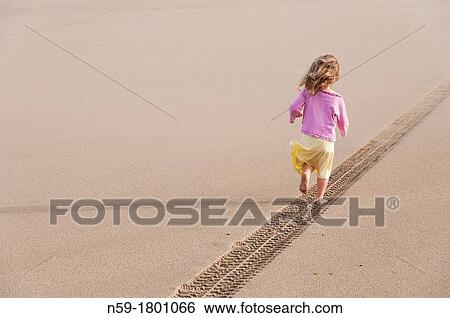 Young girl, four years old, running along a tyre track on a sandy beach View Large Photo Image Stock Photograph - Young girl, four years old, running along a tyre track on a sandy beach. Fotosearch