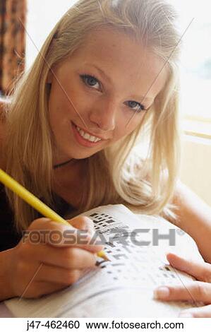 Stock Image - young girl holding a pencil doing a crossword smiling. Fotosearch