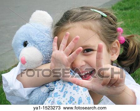 Stock Image - Young girl hugging her teddy bear and counting with fingers. Fotosearch