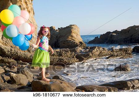 young girl in green skirt standing on rocks at the beach holding balloons View Large Photo Image Stock Photo - young girl in green skirt standing on rocks at the beach holding balloons. Fotosearch