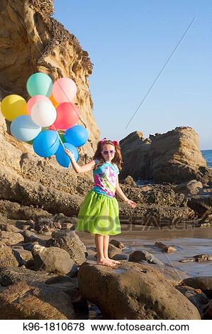 young girl in green skirt standing on rocks at the beach holding balloons View Large Photo Image Stock Photo - young girl in green skirt standing on rocks at the beach holding balloons. Fotosearch