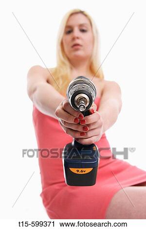 Stock Image - Young girl in her 20's holding a power tool/ drill in her hand pointing to the camera. Fotosearch