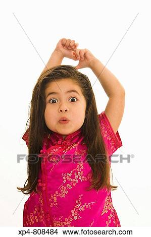 Young girl in pink clothing with long brown hair playing with facial expressions, her arms are raised above her head. View Large Photo Image Picture - Young girl in pink clothing with long brown hair playing with facial expressions, her arms are raised above her head.. Fotosearch