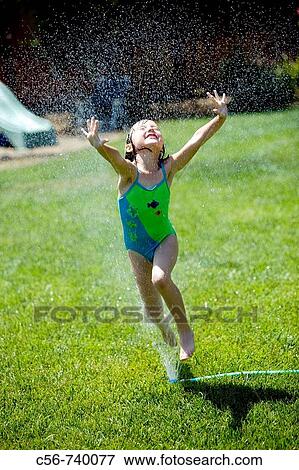 Stock Photo - Young girl leaps through yard sprinkler. Fotosearch