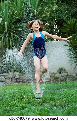 Stock Photo - Young girl leaps through yard sprinkler. Fotosearch