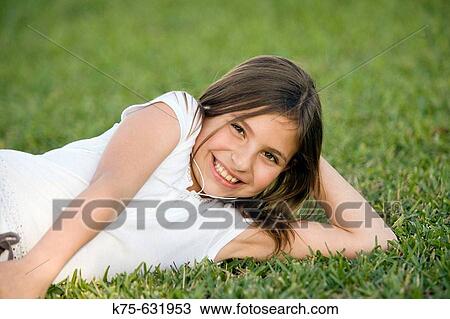Stock Image - Young girl listening to mp3 player on lawn. Fotosearch