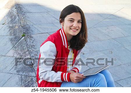 Young girl look at the camera sitting and with a digital-tablet in her hands, Spain. View Large Photo Image Stock Photograph - Young girl look at the camera sitting and with a digital-tablet in her hands, Spain.. Fotosearch