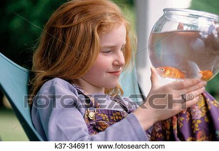 Stock Image - Young girl looking at gold fish in bowl.. Fotosearch