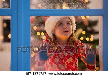 Stock Photo - Young girl looking out of the window waiting for Santa to arrive. Fotosearch