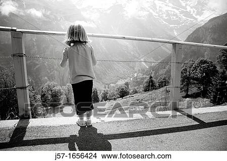 Young girl looking through a fence at a mountain scene in M? rren, Switzerland View Large Photo Image Picture - Young girl looking through a fence at a mountain scene in M? rren, Switzerland. Fotosearch