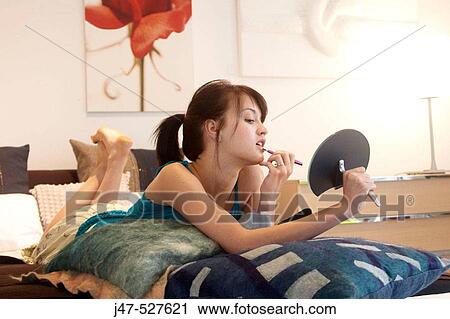 Stock Image - young girl lying on a bed with mirror and make-up brush. Fotosearch